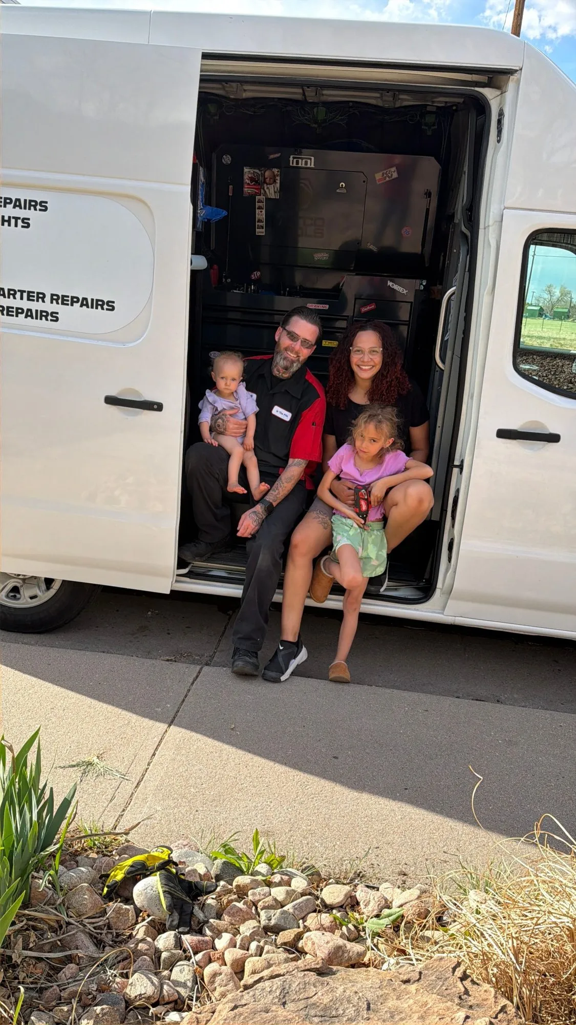 Jeff sitting in the side door of the In The Pits service van with his wife and two kids