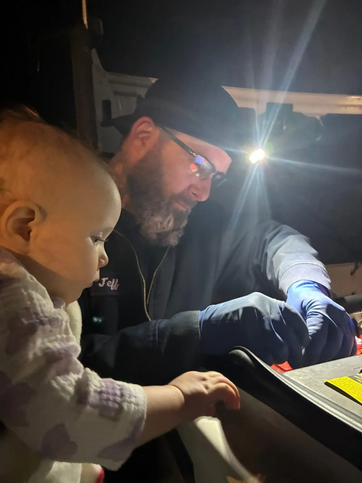 Jeff working under a hood at night by headlamp while his youngest looks on