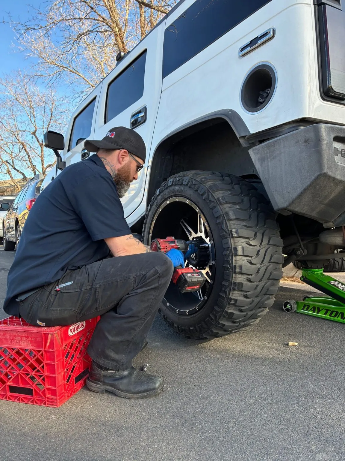 Jeff of In The Pits replacing a wheel on a lifted Hummer H2 with an impact wrench, right in the customer's parking spot